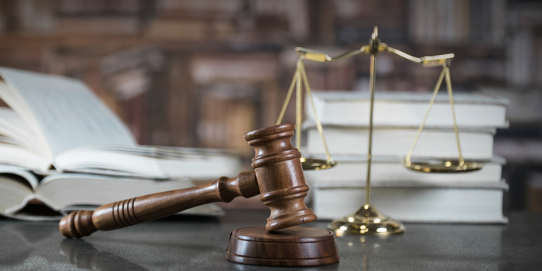 Εικόνα ενός δικαστικού σφυριού που βρίσκεται σε ένα γραφείο και στο βάθος υπάρχουν μια θολή κλίμακα και θολά λευκά βιβλία
